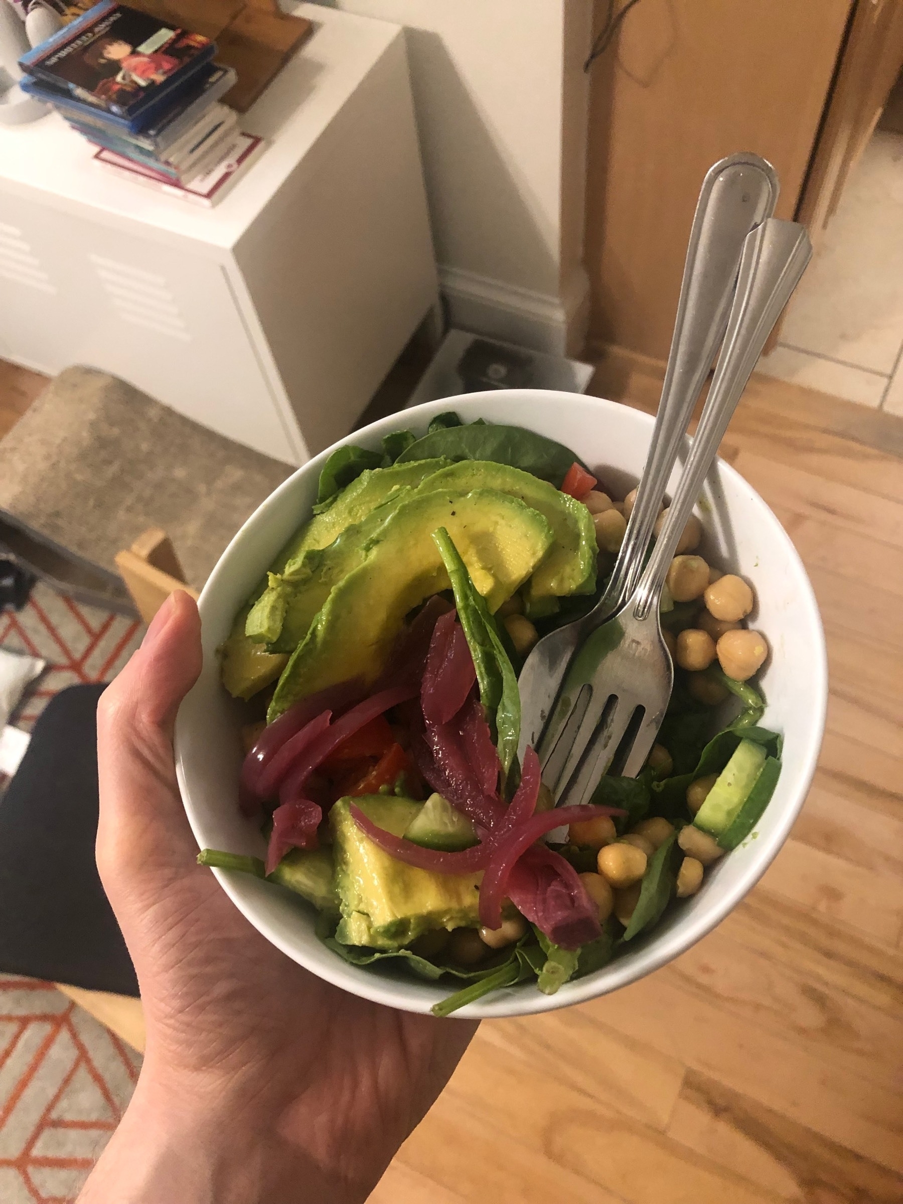 A bowl of spinach, chick peas, pickled red onion, Persian cucumbers, and avocado